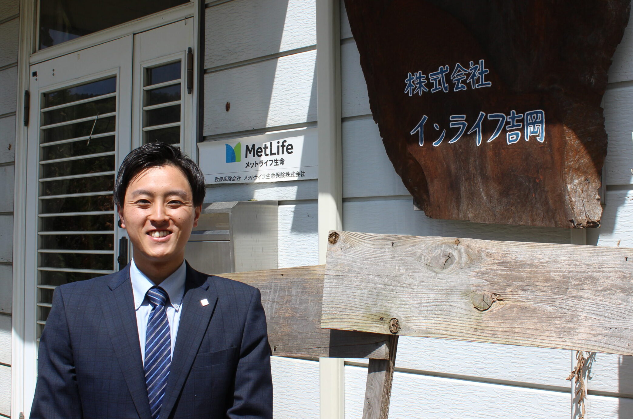 株式会社インライフ吉岡　吉岡睦生氏。店舗前で笑顔。